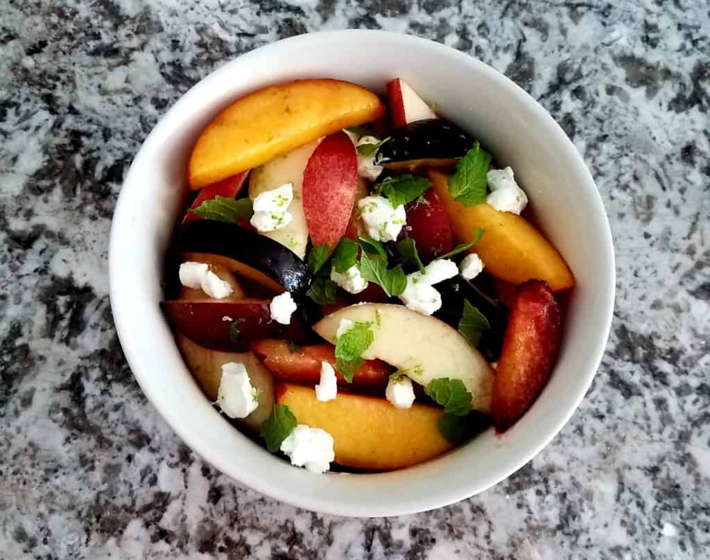 A bowl of stone fruit salad with goat cheese and mint.