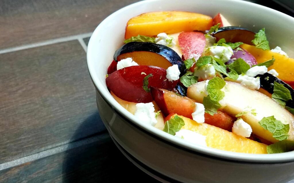 A bowl of delicious fruit salad featuring fresh stone fruits, goat cheese, and mint.