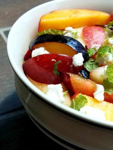 A bowl of delicious fruit salad featuring fresh stone fruits, goat cheese, and mint.